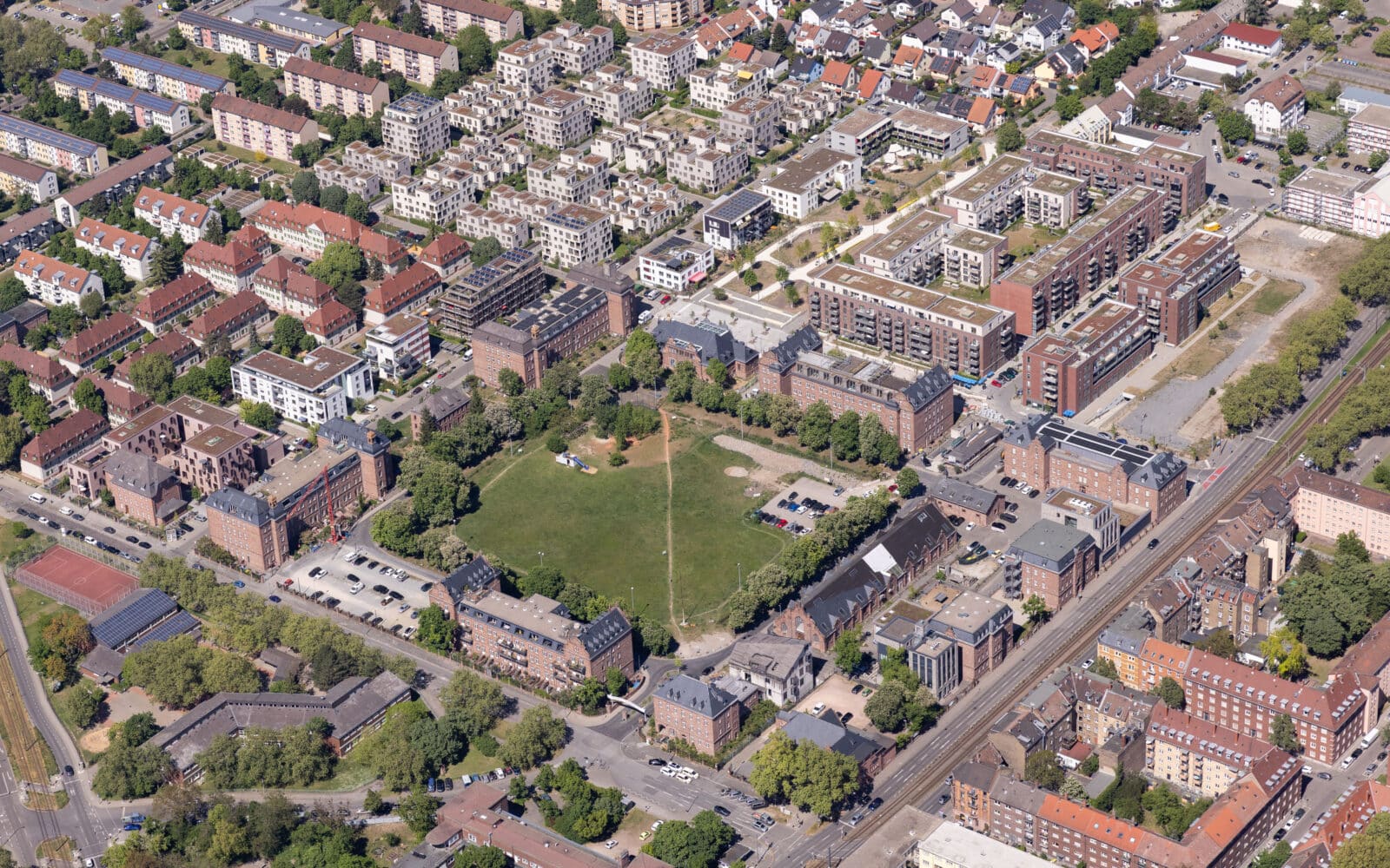 KI-basierte Bildbeschreibung | Luftaufnahme eines Stadtviertels mit Wohngebäuden, Grünflächen, Straßen und geparkten Autos, die im gesamten Gebiet zu sehen sind.